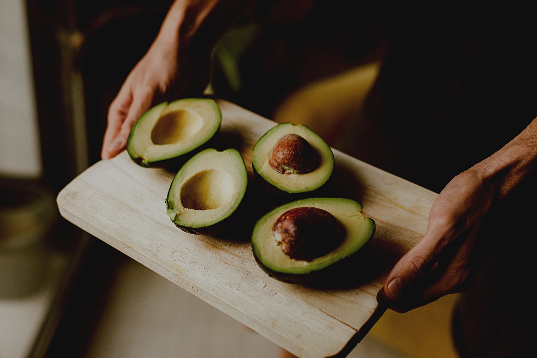 Close-Up Shot of a Person Holding a Wooden Tray with Sliced Avocados